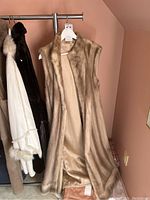 Long ladies mink vest in natural light brown fur, hanging on rack showing full length and inside satin lining.