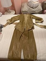 Gold metallic Billtice pantsuit laid out on bed showcasing texture and cut of jacket and pants, with belt beside jacket.