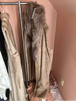 Full side view of the lined leather vest hanging on a rack showing the patchwork suede leather and the plush fur collar.