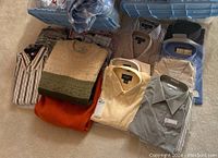 Top view photo of folded mens XL shirts and knit sweaters in various colors and patterns on carpet
