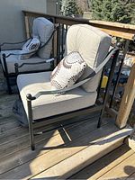 Two metal patio chairs with beige cushions and patterned throw pillows on wooden deck