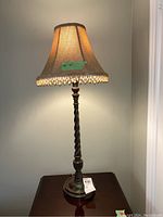Full view of one illuminated table lamp showing fabric shade with beaded trim and carved wood base