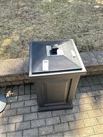 Top view of black resin patio storage bin with lid and knob, showing wear.