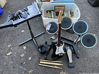 Photo of entire Rockband 3 game set including drum set with drumsticks, guitar controller, keyboard, microphone, and foot pedal on outdoor surface.