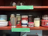 Shelf with multiple scented candles, pewter cup, and ceramic decorative candle holder.