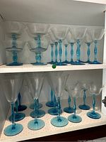 Full view of 26 piece crystal stemware collection showing four different glass sizes with distinctive blue stems and bases on two shelves.