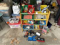 Full view of wooden shelf with colored plastic storage buckets containing tools, Ryobi drill and accessories laid out in front.