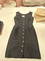 Front view of black sleeveless formal dress by Deja Paris with decorative pearl and diamond style buttons.