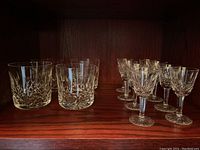 Overview of 4 lowball tumblers on left and 8 small stemware glasses on right displayed on shelf