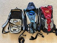 Top view showing front of three CamelBak hydration backpacks with visible hydration hose and bladder in middle backpack