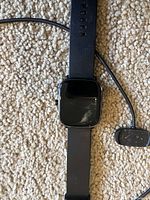 Photo of black Amazfit GTS2 Mini smartwatch lying on carpet with charging cable beside it.