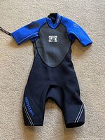 Front view of a black and blue short-sleeve, short-leg wetsuit for juniors size 8 with Bodyglove branding on front.