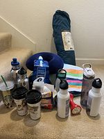 Camping equipment lot showing water bottles, travel mugs, pillow, vitamins, bottled drinks, flashlight and other accessories