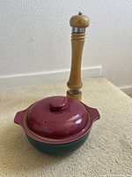 Denby covered bowl in maroon and blue placed next to a tall wooden peppermill on a carpeted floor