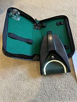 Golf putting machine in open carrying case showing the green putting surface and black plastic body