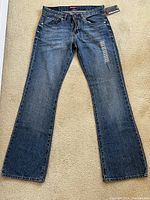 Front view of Union Bay denim jeans laid flat on carpet, showing medium blue wash with mild distressing and original tags on waistband.