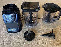 Full view of Ninja blender base, two pitchers with lids and blade assemblies, extra blade, and mixing cup lid.