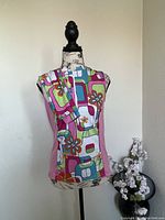 Front view of sleeveless Springfield Sheila Moon cycling jersey on mannequin with matching arm warmers draped over shoulder. Jersey has pink side panels and vibrant geometric floral print front.