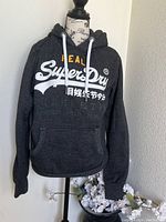 Front view of the dark grey Superdry heavyweight hooded sweatshirt showing the white and yellow printed logo and front pouch pocket.