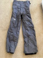 Front view of gray The North Face Gore-Tex ski/snowboard pants laid flat showing logos and zippers.