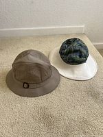 Two hats on carpet: beige gardening hat with buckle and reversible floral/white hat