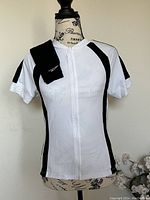 Front view of white and black short-sleeve cycling jersey displayed on mannequin with black arm warmers draped over