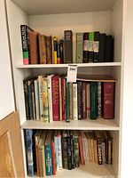 Bookshelf with a mix of old and newer plathardcover and softcover books including cookbooks, dictionaries and cookbooks.