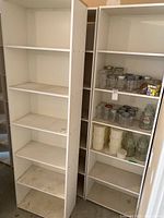 Photo shows three white tall bookshelves with 5 fixed shelves each, one holding various jars and containers. Signs of wear, dirt, and damage evident