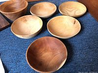 Six wooden bowls with varying wood types and grain patterns displayed on a blue carpet.