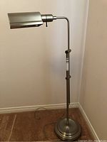 Full view of the metal adjustable floor lamp standing on carpet near a wall.