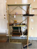 Metal shelving unit holding assorted hand tools and hardware, broom and push broom leaning on side