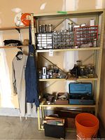 Metal shelving unit holding multiple plastic drawer organizers with hardware, glass jars with screws/nails, blue plastic toolbox, hanging Lee Valley apron and coveralls, and orange bucket on floor