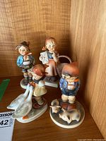 Four Goebel Hummel figurines displayed together on wooden surface.