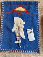 Front view of blue wool wall hanging with embroidered native figure and sun motif, includes a MaxSold tag with lot number 150