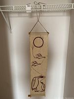 Full view of vertical woven fabric wall hanging hanging on a wire shelf. Light beige fabric with dark maroon screen printed birds and sun design.
