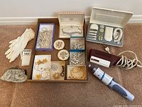 Full lot overview showing assorted costume jewelry in boxes, small lace handbag, white gloves, Braun steam curing iron, Kenmore hair dryer, and Philips lady shaver on carpet.