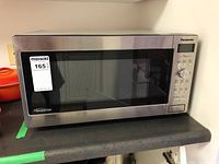 Panasonic microwave oven on a kitchen counter featuring a stainless steel finish with black glass door and visible maxsold sticker.