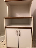 View of the microwave cart front showing the two-door cabinet with woodgrain trim handles and open shelf above.