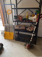 Photo of outdoor gardening items on shelving unit including large yellow shovel, smaller metal shovel, various pots, soil bags and hand tools. Shelving unit not included.