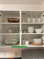 Wide view of shelf with vintage Pyrex mixing bowls, glass carafes, various glass bakeware and serveware items.