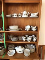 Full view of the china collection on wooden shelves showing various plates, bowls, cups, and serving dishes.