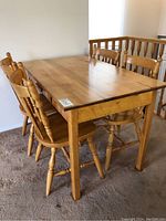 Photo showing solid wood rectangular dining table with integrated drawer and four matching spindle back dining chairs on carpeted floor.