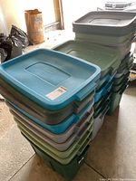 Stacked assorted plastic storage bins with lids in green, blue, and gray colors, multiple sizes visible.