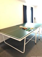 Side view of the green ping pong table fully set up with paddles, nets, and balls on top.