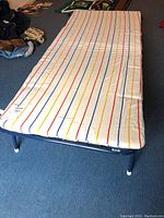 Full view of the twin folding cot with foam mattress covered in a striped fabric cover in red, yellow, and blue on white.