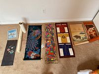 Full view of assorted wall hangings spread on floor including painted velvet peacock, fabric appliqué floral piece, quilted kimonos, vintage map, and others