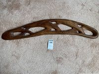 Full view of the front side of the rosewood carving showing its smooth finish and organic hollow cutouts on a beige carpet background.