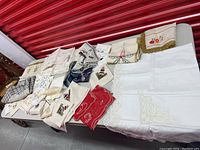 Photo showing multiple assorted antique handmade needlepoint and crochet linens in various colors and designs laid out on a table.
