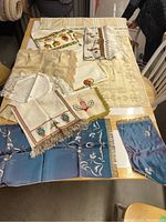 Photo of assorted hand needlepoint lace linens in various sizes and colors laid out on the table.