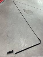 Full length view of the long metal drain snake tool with crank handle on one end, showing the rod on a floor surface.
